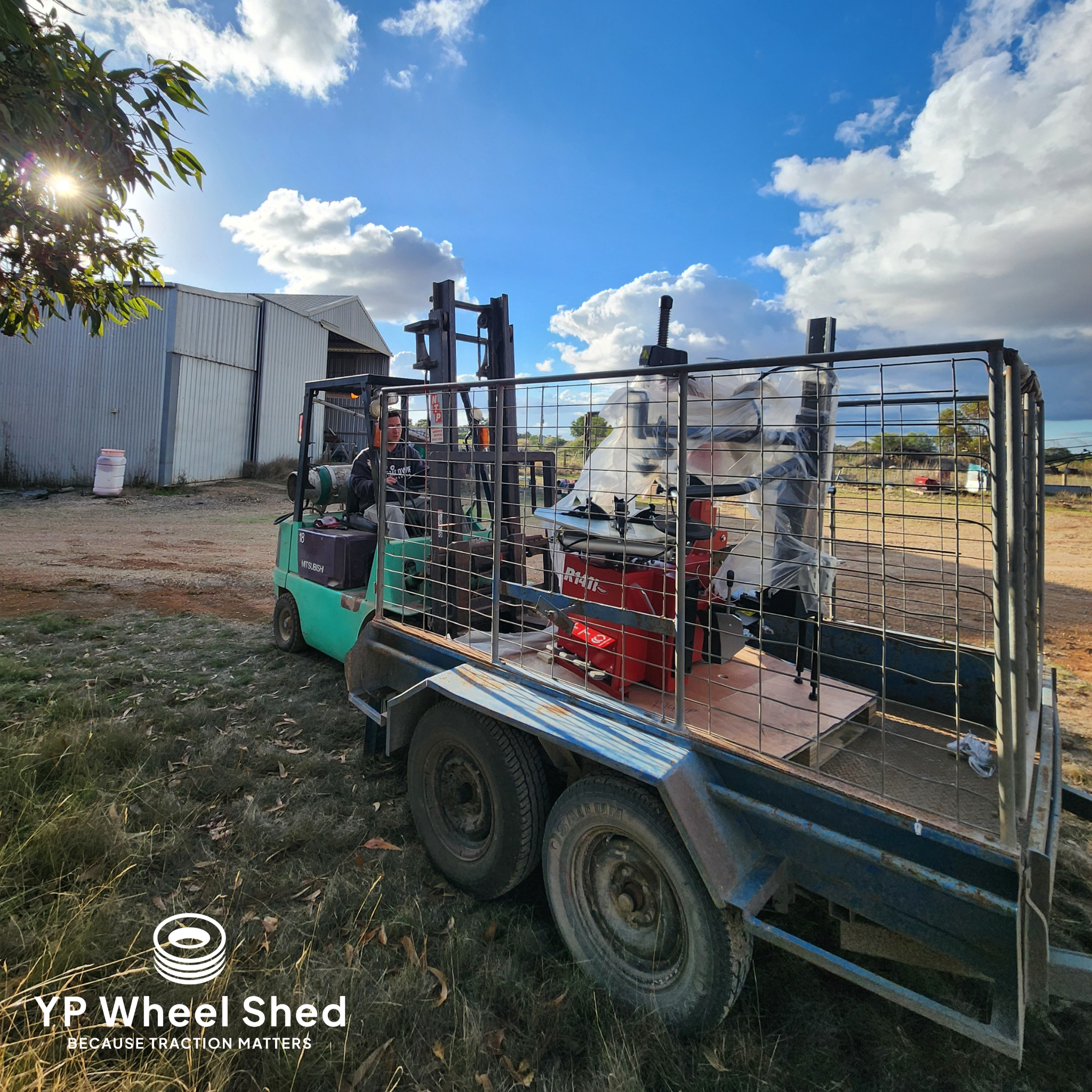 A forklift loading a red tyre changing machine onto a caged trailer outside the shed at Minlaton