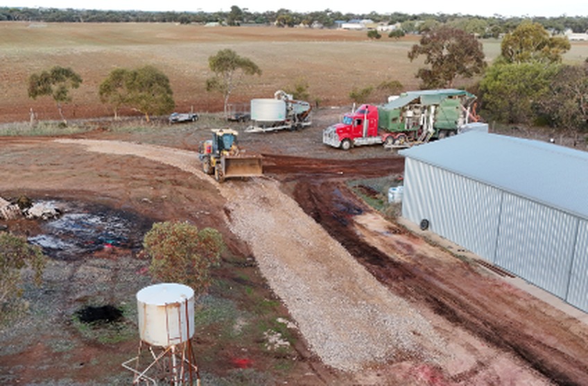 Looking down on a farm job site, a red prime mover and a loader working beside a shed with cropped paddocks running to the horizon